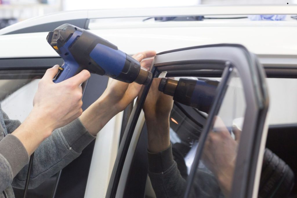 A technician uses a heat gun on a car window frame, preparing to install or adjust the rubber seal around the glass.
