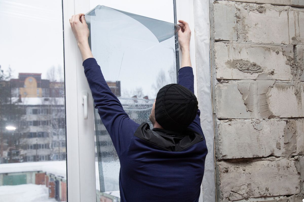 A man carefully installs a window screen onto a window frame, ensuring a secure fit. 